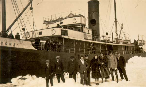 Seven men and two women standing near the rescue ship  S.S. "Sagona." - Sept hommes et deux femmes se tenant près du S.S. "Sagona."